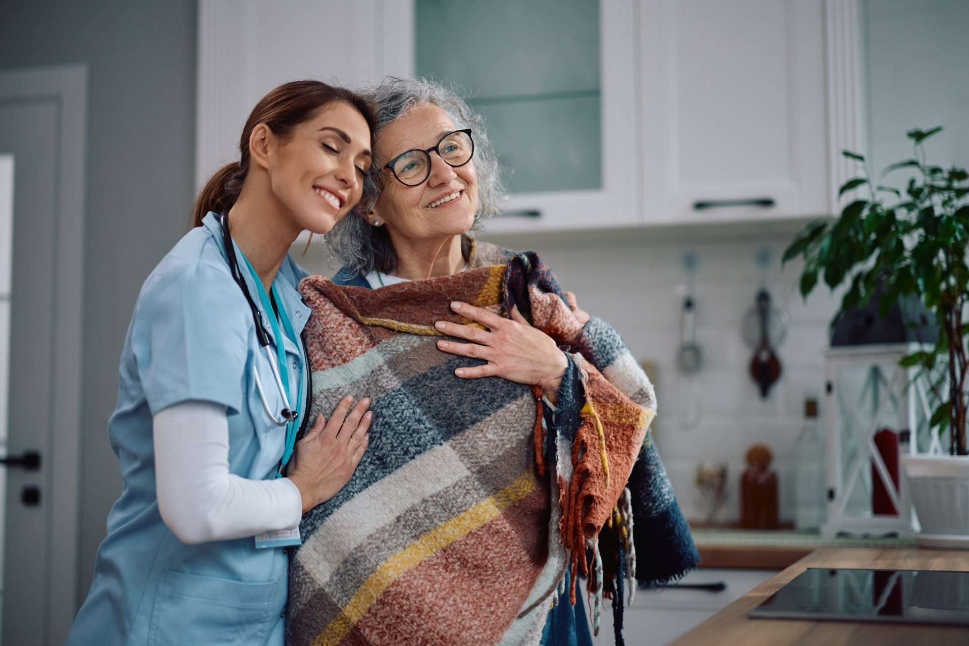 Loving Senior Woman And Her Caretaker In The Kitchen.